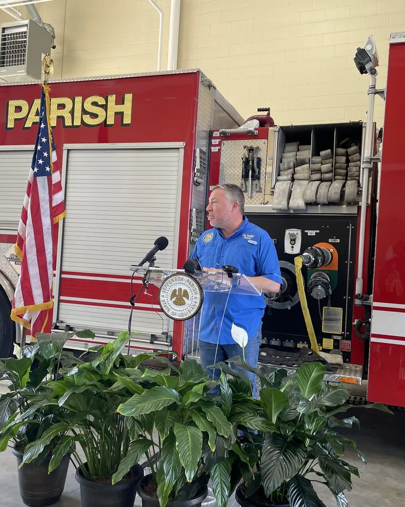 Tim Baudier speaking at a Jefferson Parish podium beside a fire engine